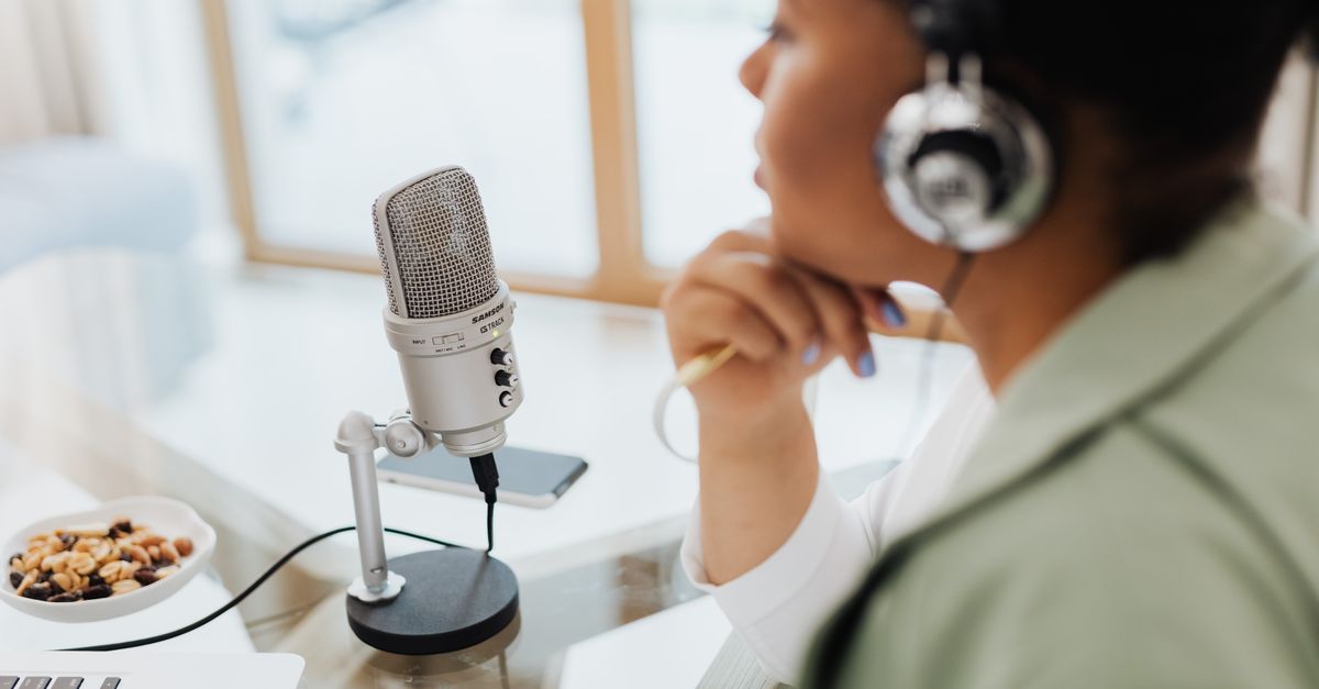 Woman using laptop and microphone for podcasting at home.